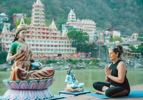 Woman meditating beside a statue by the Ganges in Rishikesh, capturing spirituality and serenity.